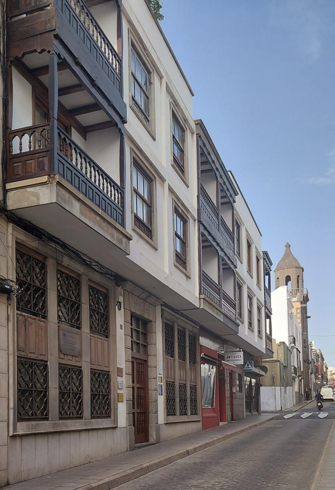 Una calle con un edificio blanco con balcones y una torre de iglesia al fondo.