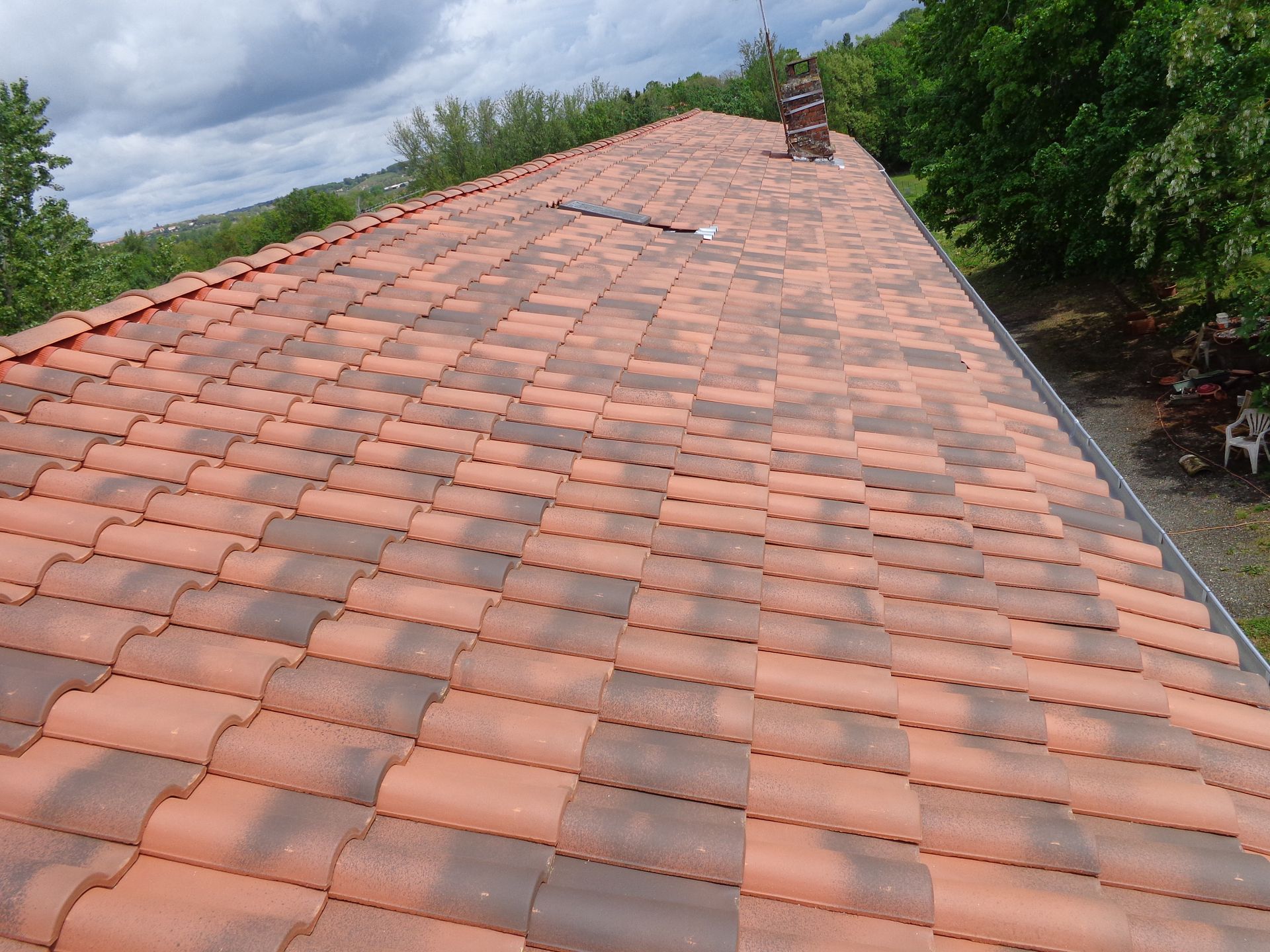 Pose de tuiles sur un long toit avec cheminée.