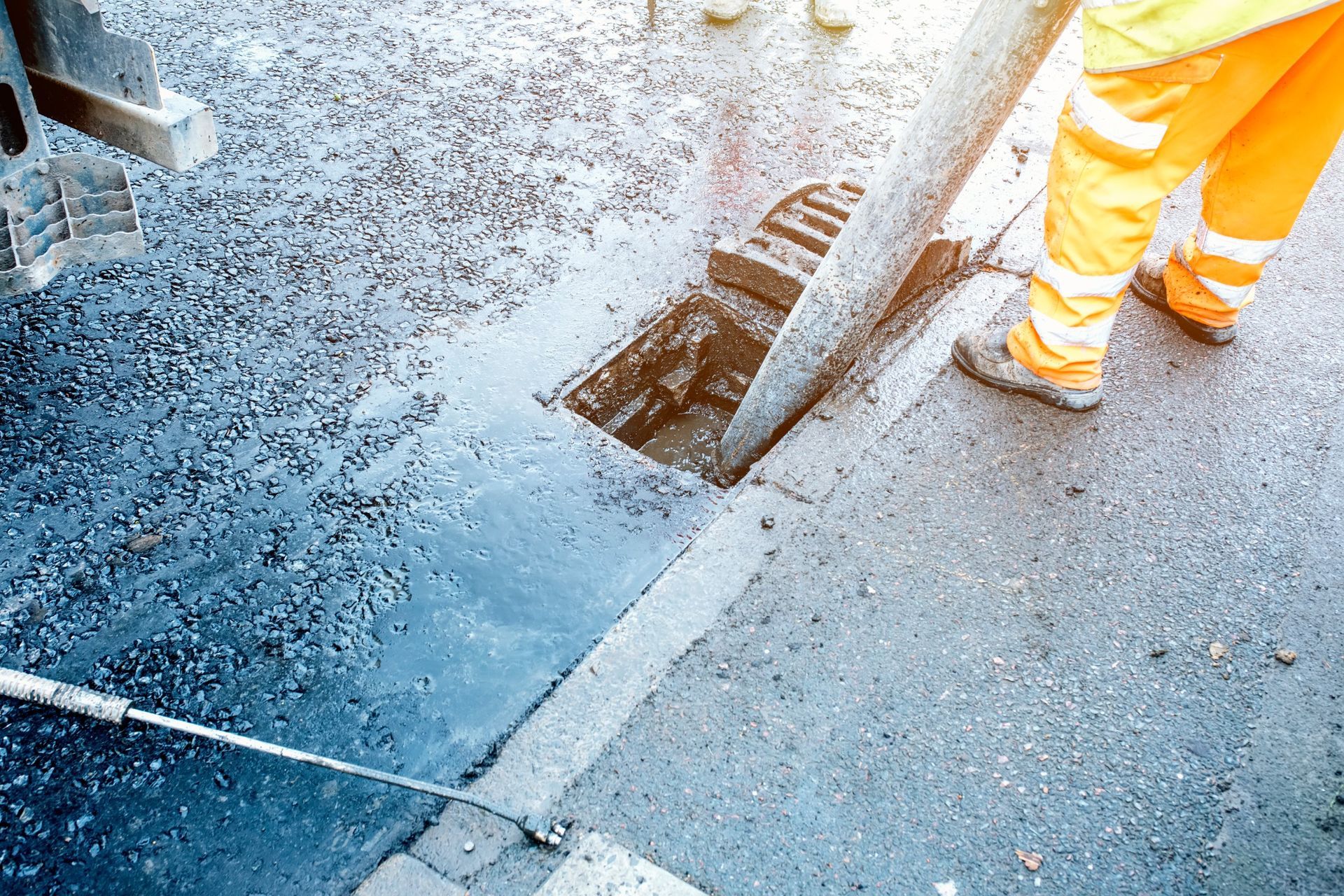 Un hombre está parado junto a una tapa de alcantarilla al costado de una carretera.