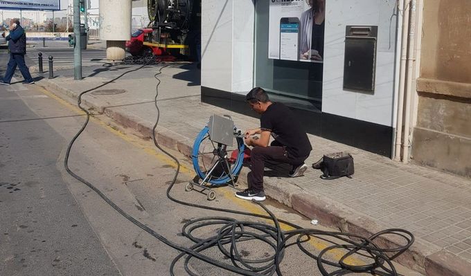 Un hombre está sentado en la acera trabajando en un neumático.