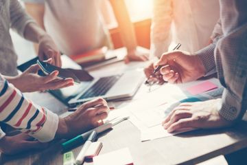 Des personnes collaborent autour d'une table, travaillant avec un ordinateur portable, des documents et des stylos dans un bureau bien éclairé.
