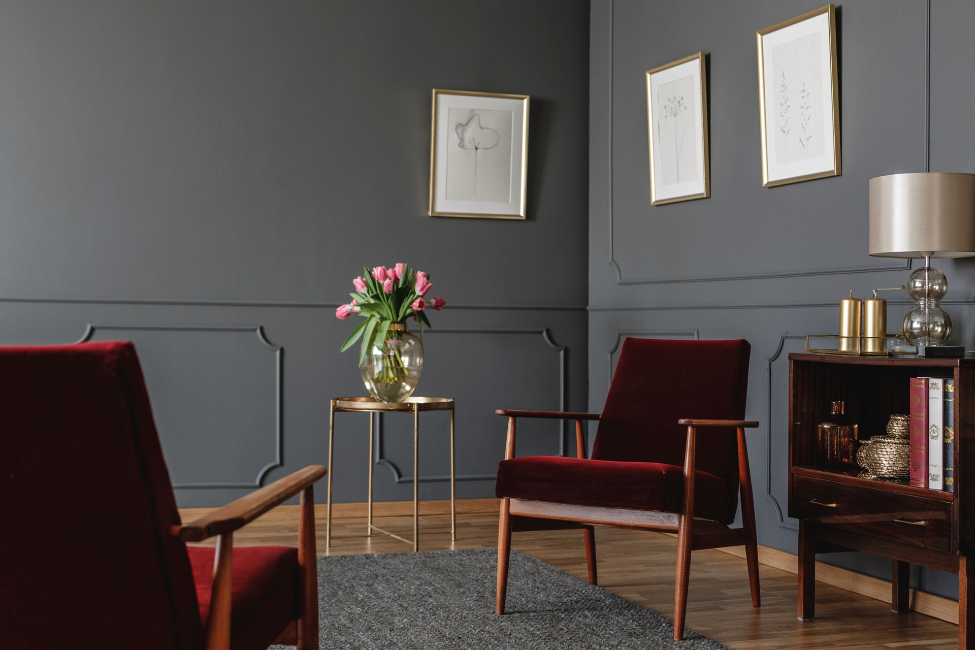 Deux fauteuils en velours rouge foncé se font face dans une pièce aux murs lambrissés gris anthracite, avec une petite table et une lampe.