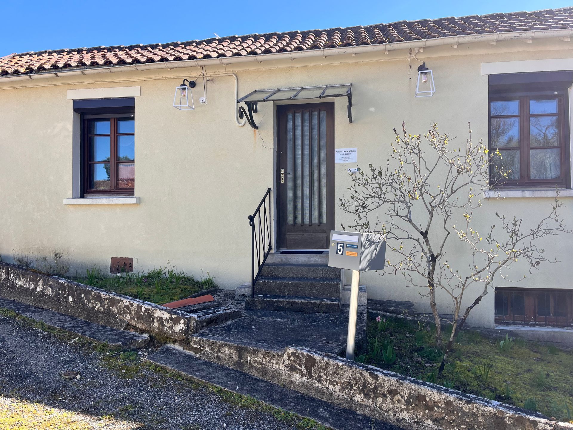 Sur un bureau, un tableau à cadre argenté porte l'inscription PSYCHOSOCIAL en lettres de carrelage, à côté de fleurs violettes et de verres.