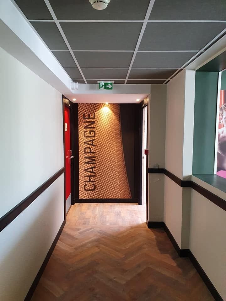 Couloir avec parquet et plafond sombre menant à un panneau éclairé portant l'inscription CHAMPAGNE.