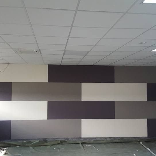 Mur décoratif en toile tendue, constitué de panneaux rectangulaires alternant les couleurs gris clair, gris foncé, blanc et anthracite.