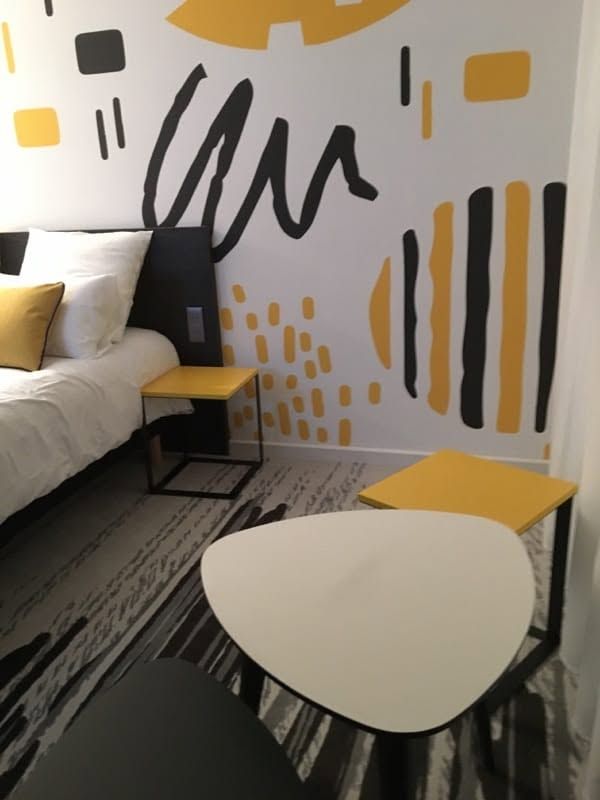 Chambre moderne avec un mur en toile tendu imprimée ; motifs graphiques noirs et jaunes.