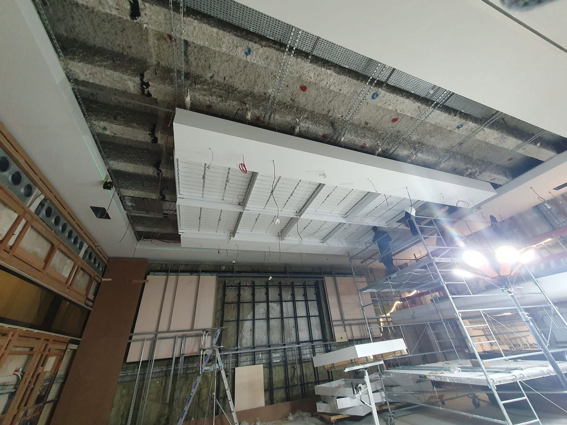 Chantier de construction avec plafond apparent, échafaudages et échelle dans une pièce en rénovation.