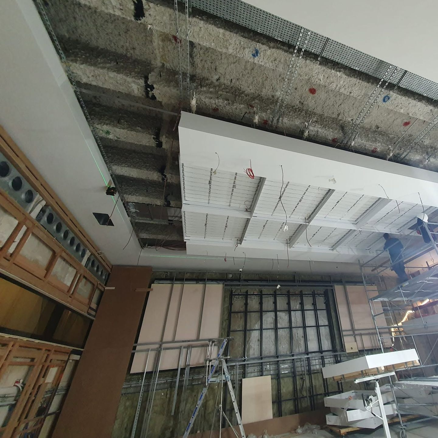 Chantier de rénovation avec plafond apparent, échafaudages et matériaux de construction dans une pièce partiellement aménagée.