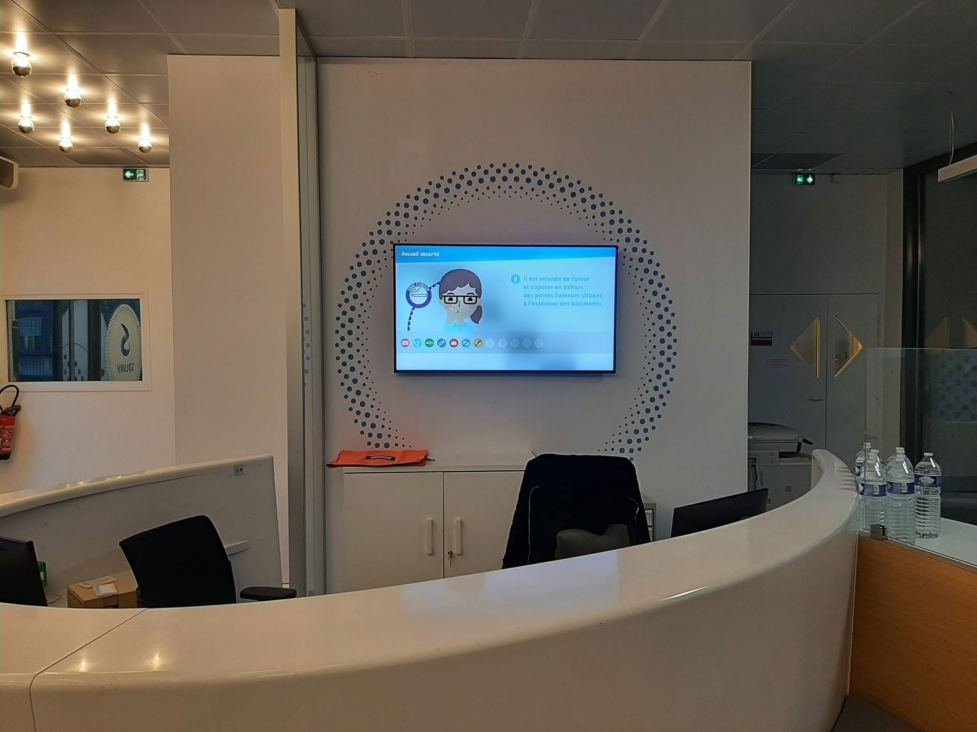 Espace d'accueil moderne avec un bureau blanc incurvé et un écran sur un mur imprimé.