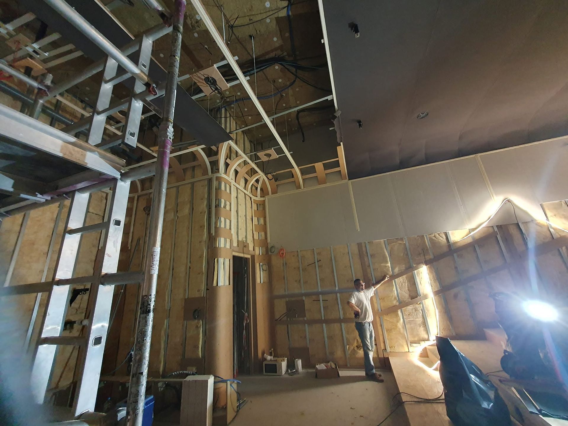 Chantier de construction intérieure avec charpente apparente, échafaudages et travaux de plafond en cours.
