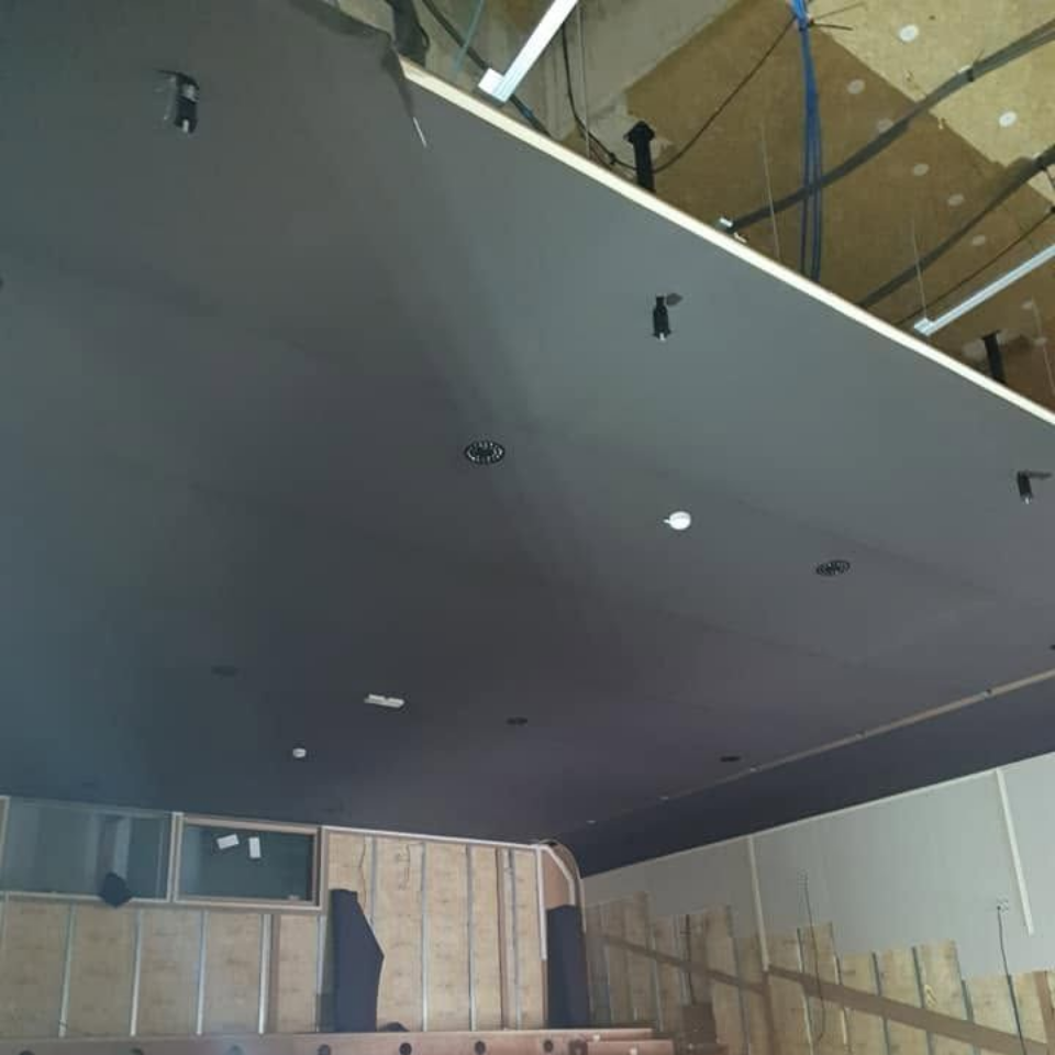 Plafond tendu acoustique partiellement installé dans une salle avec gradins en construction.