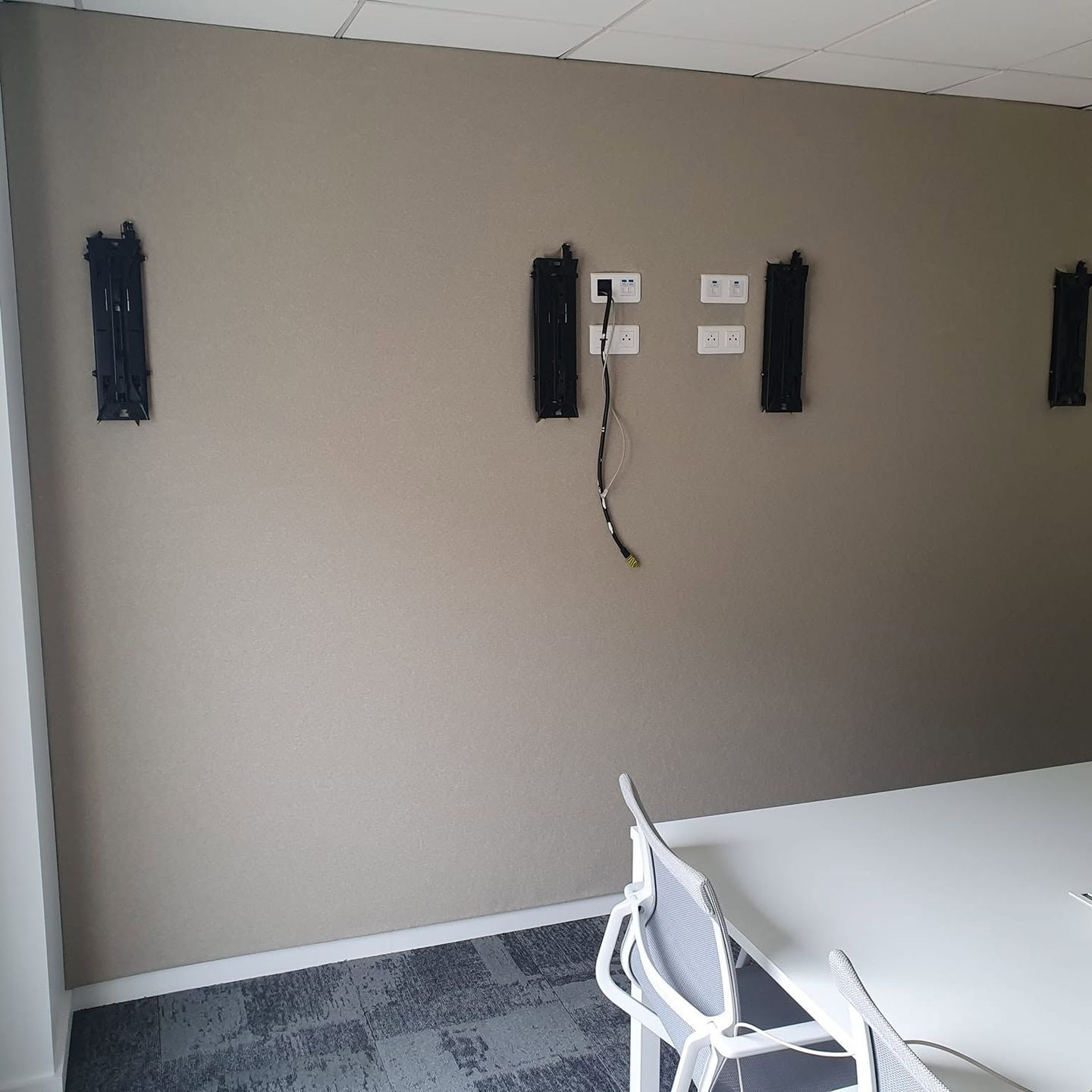 Salle de conférences avec un mur en toile beige, des supports muraux d'écrans et une table et une chaise blanches au premier plan.