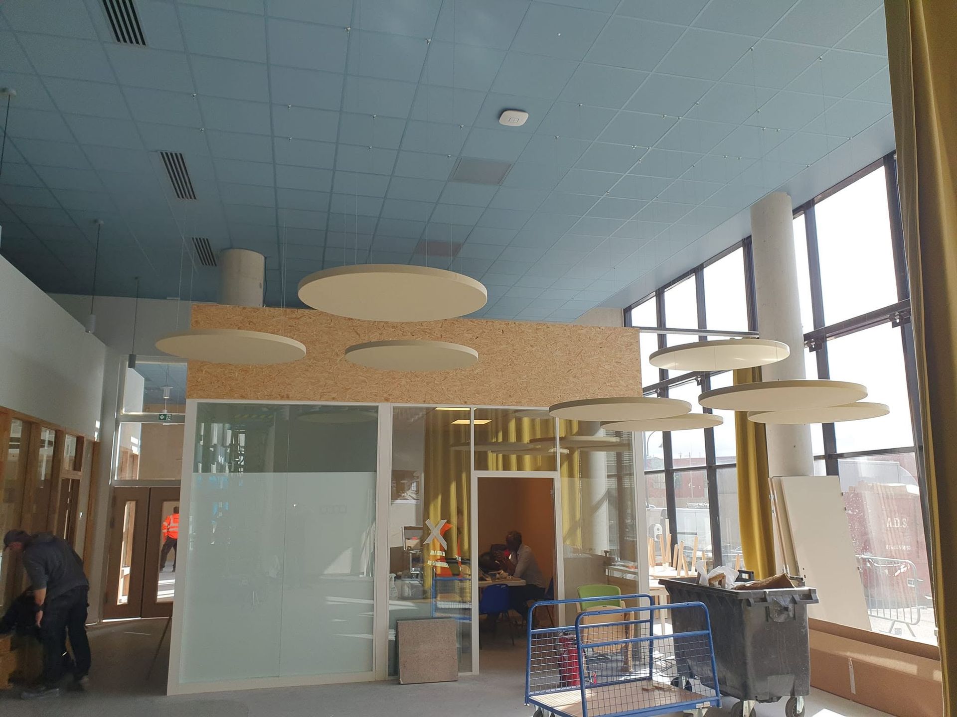Hall d'entrée moderne avec baffles acoustiques suspendus au plafond, parois vitrées.