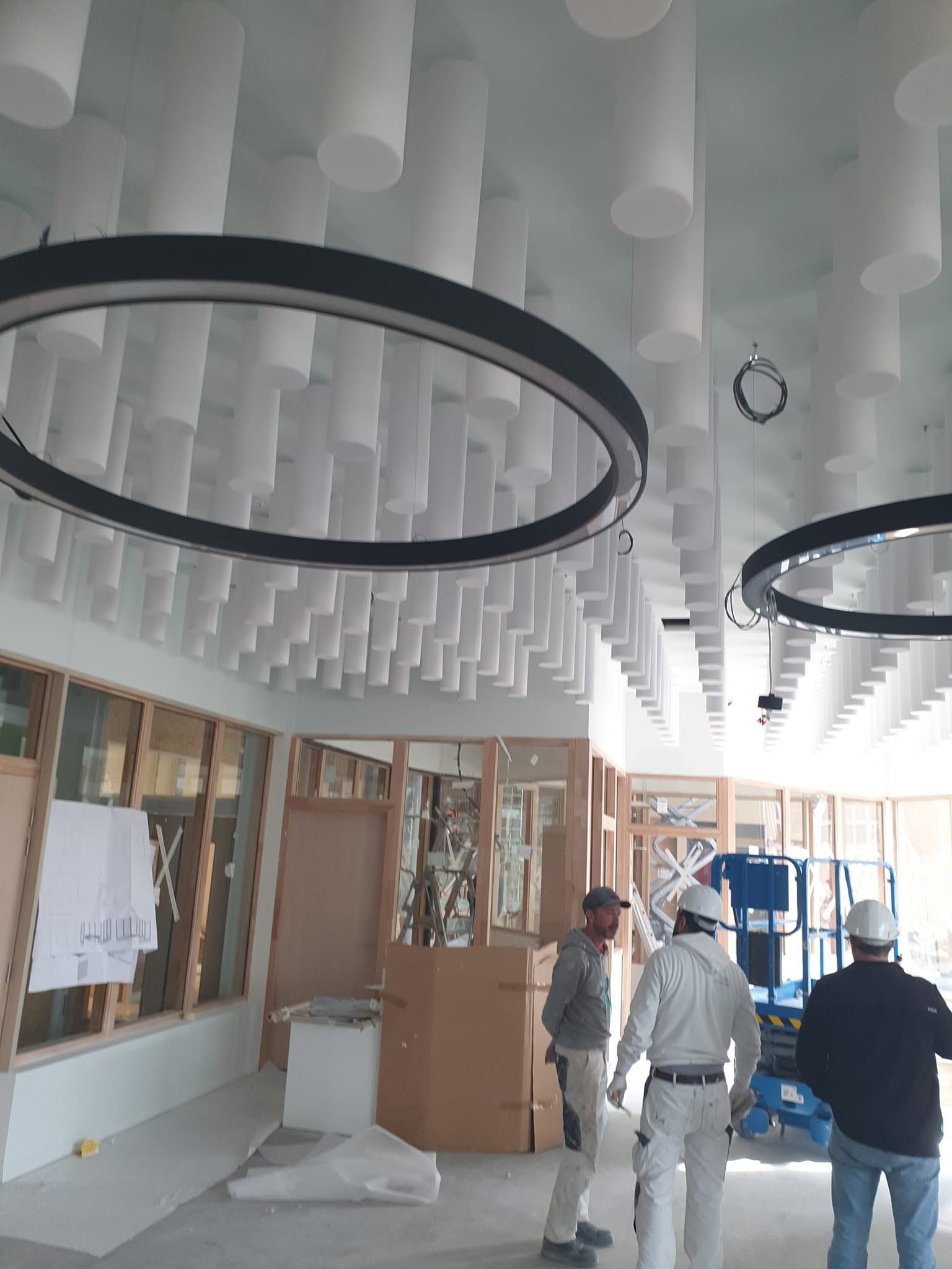 Espace intérieur en cours d’aménagement avec plafond acoustique suspendu et luminaires circulaires.