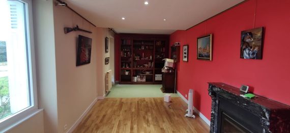 Salon avec plafond tendu à LED, mur d'accent rouge, tableaux encadrés, cheminée et fenêtre à gauche.