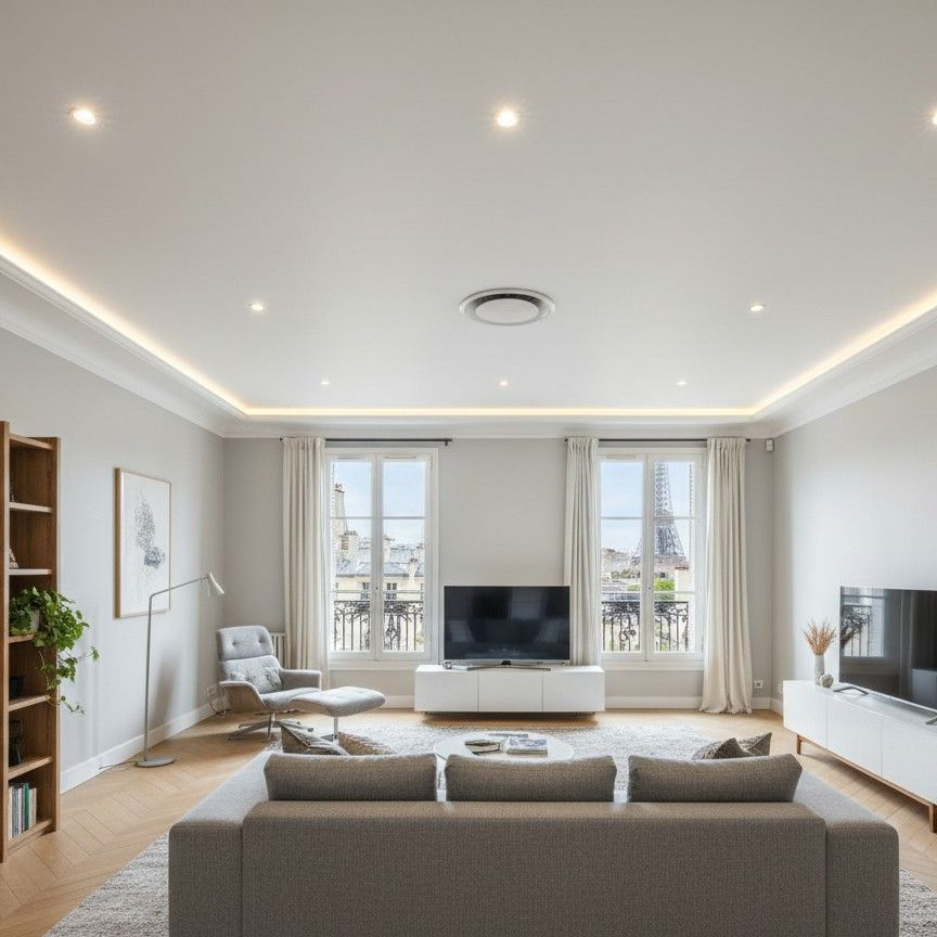 Salon moderne et lumineux avec canapé gris, télévision, grandes fenêtres, parquet chaleureux et plafond tendu avec spots encastrés.