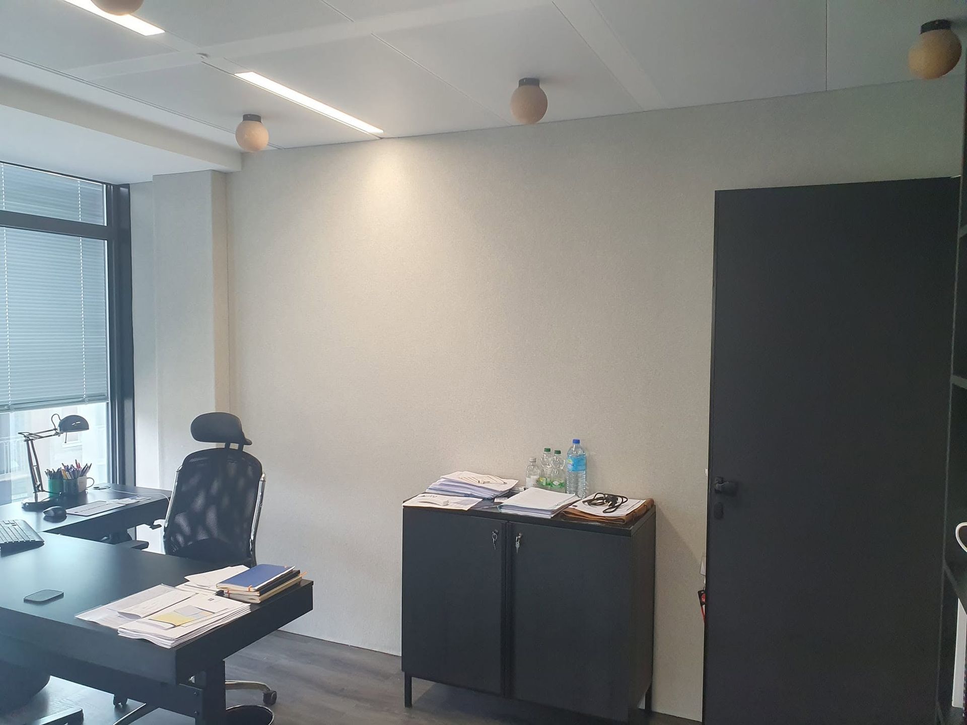 Bureau vide avec un bureau, une armoire et une chaise près d'une grande fenêtre et d'un mur acoustique en tissu tendu.