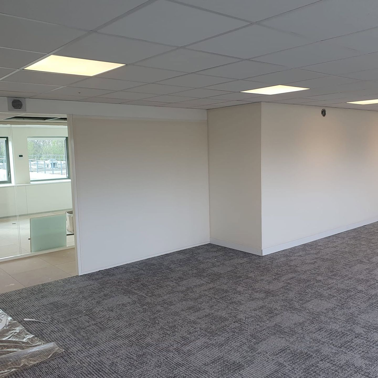 Des bureaux vides avec moquette grise, murs blancs et éclairage LED au plafond.