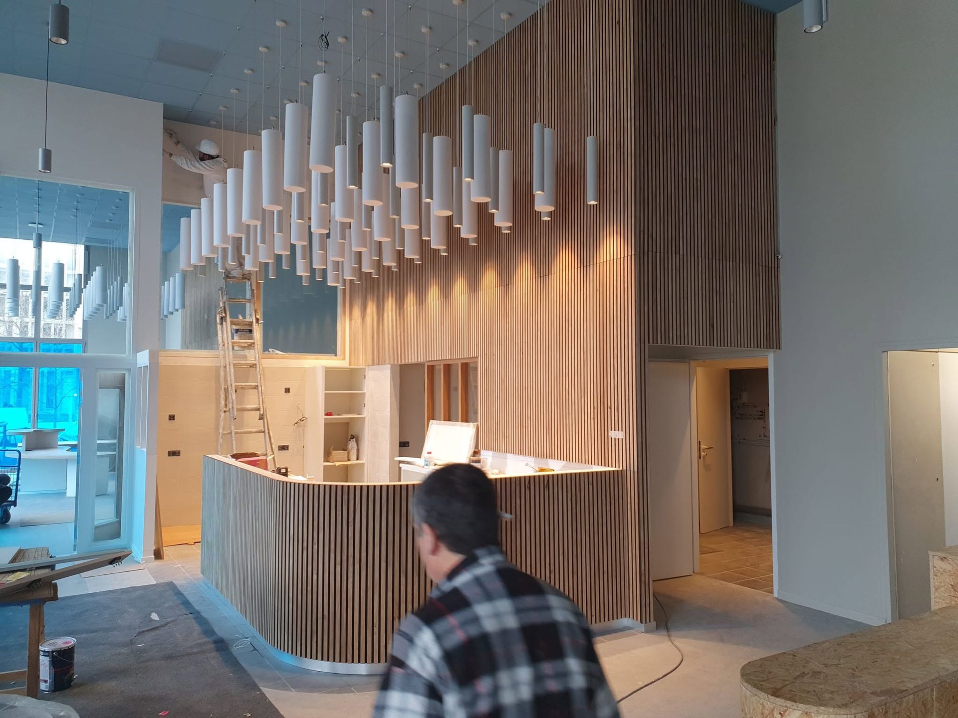 Comptoir d'accueil moderne avec panneaux acoustiques et suspensions blanches dans un hall lumineux.