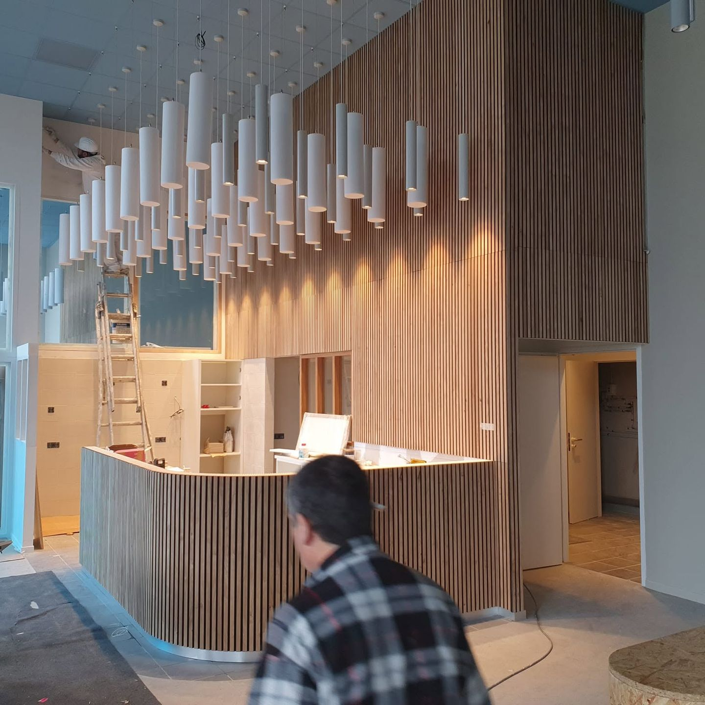 Comptoir d'accueil moderne avec panneaux acoustiques et suspensions blanches dans un hall lumineux.