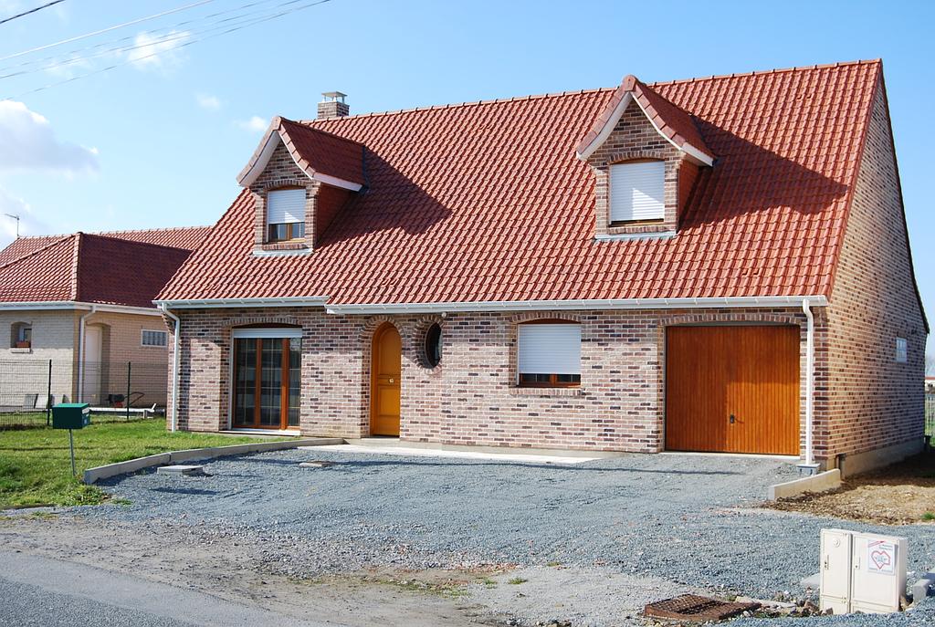 Maison individuelle en brique sur ton de rouge avec menuiserie en bois brut et volets roulants en PVC
