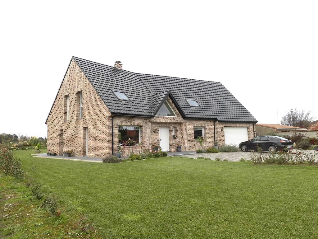 Maison neuve en briques de plusieurs teintes dont la porte d'entrée est surmontée d'une fenêtre à la forme triangulaire