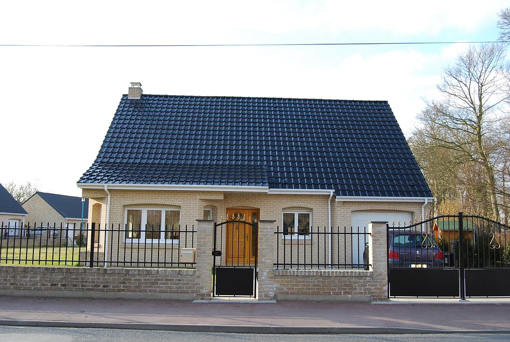 Maison dont le terrain est délimité par un muret en brique ainsi qu'une grille et des portails en fer noir