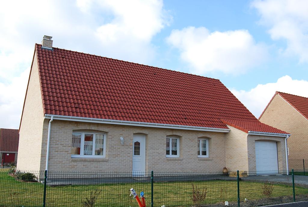 Maison individuelle avec toit en tuile rouge possédant 3 fenêtres et une porte de garage à l'avant