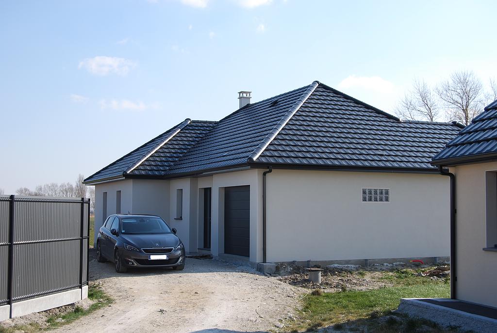 Maison individuelle reculée par rapport à la route dont les menuiseries extérieures et le toit sont de couleur noire