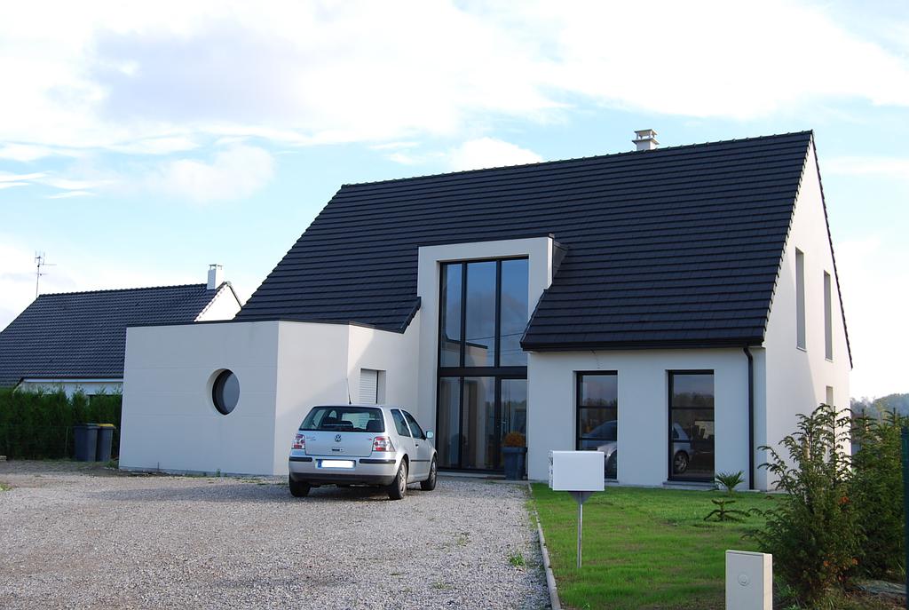 Maison individuelle moderne avec grande baie vitrée en entrée. Une voiture est garée devant.