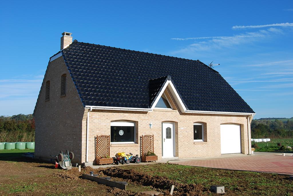 Maison individuelle en brique et menuiseries blanches, un terrain de jardinage est en façade