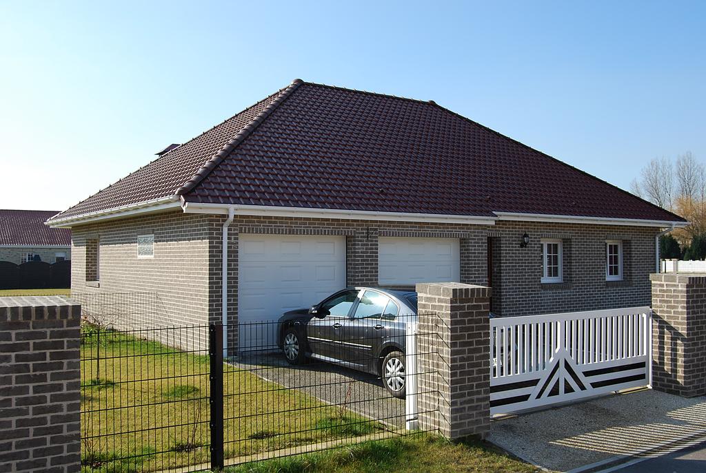 Maison individuelle en briques marrons possédant deux portes de garage et un portail en PVC