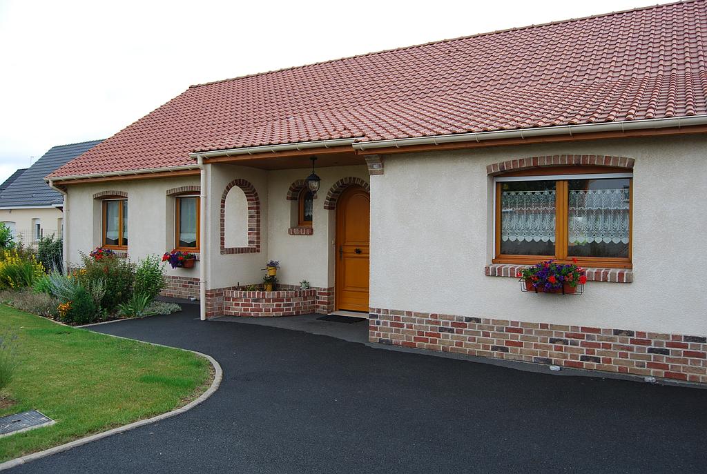 Maison individuelle dont le terrain avant est aménagée avec une entrée goudronnée et des espaces verts fleuris