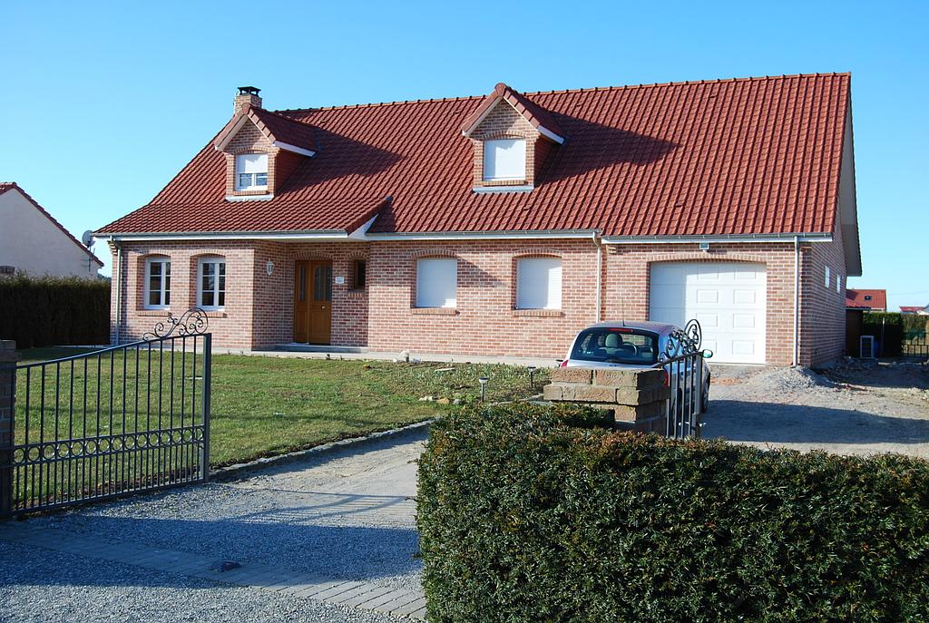 Grande maison individuelle en brique rouge dont l'entrée est délimitée par un portail en fer forgé