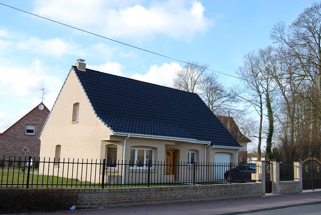 Maison individuelle avec toit en tuile noire, une grille en fer peinte en noir délimite le terrain.