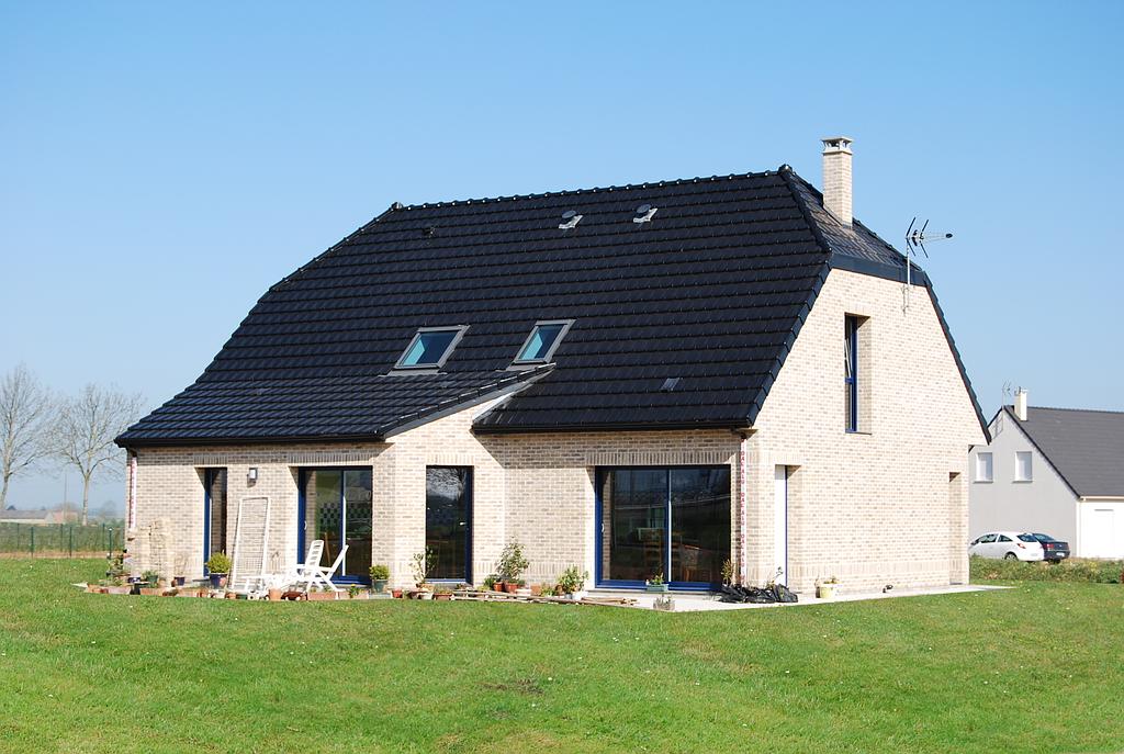 Vue sur l'arrière d'une maison individuelle équipée de plusieurs baies vitrées donnant sur un espace vert non arboré