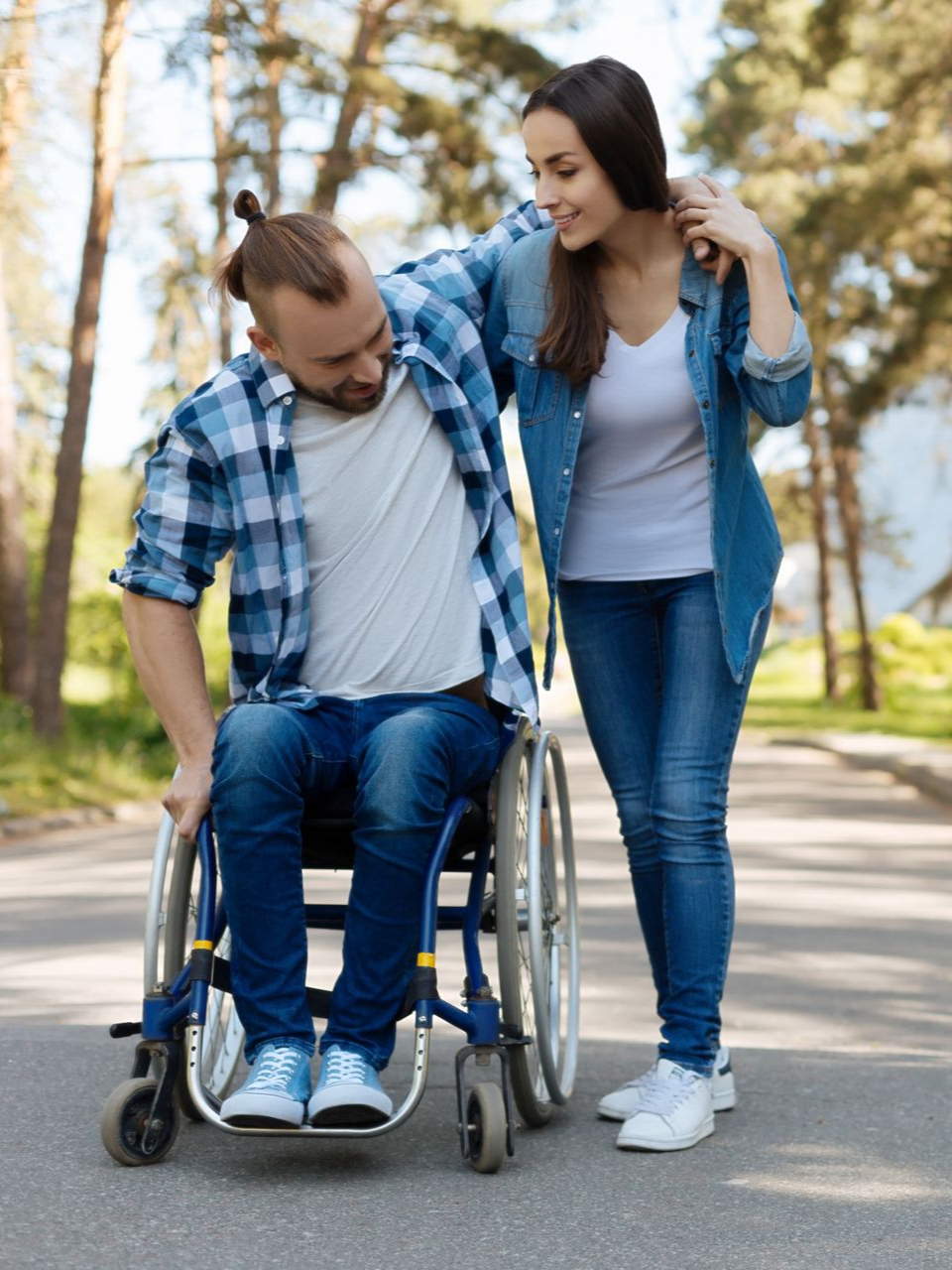 Un homme en fauteuil roulant sourit tandis qu'une femme l'aide 