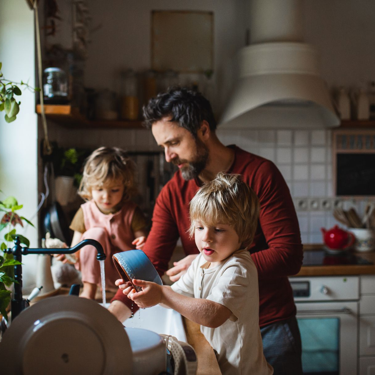 Un père et ses deux jeunes enfants font la vaisselle dans une cuisine.