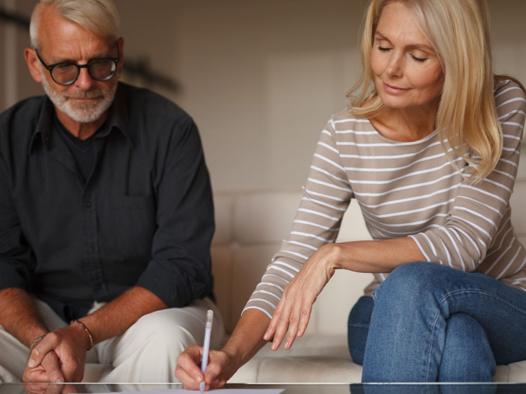 Une femme âgée signe des documents, assise à côté d'un homme