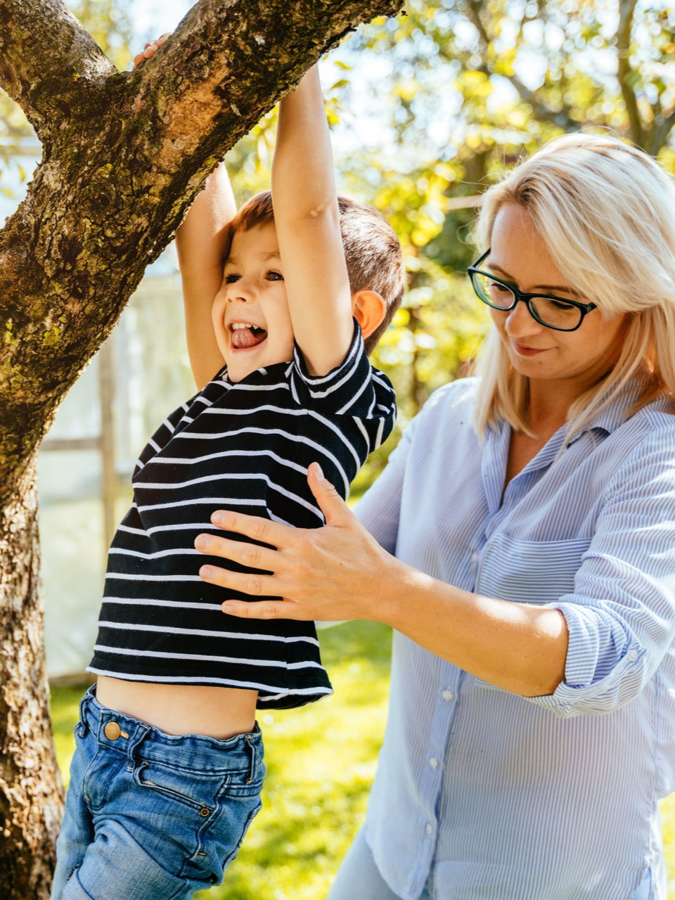 Garçon suspendu à une branche d'arbre, aidé par une femme souriante
