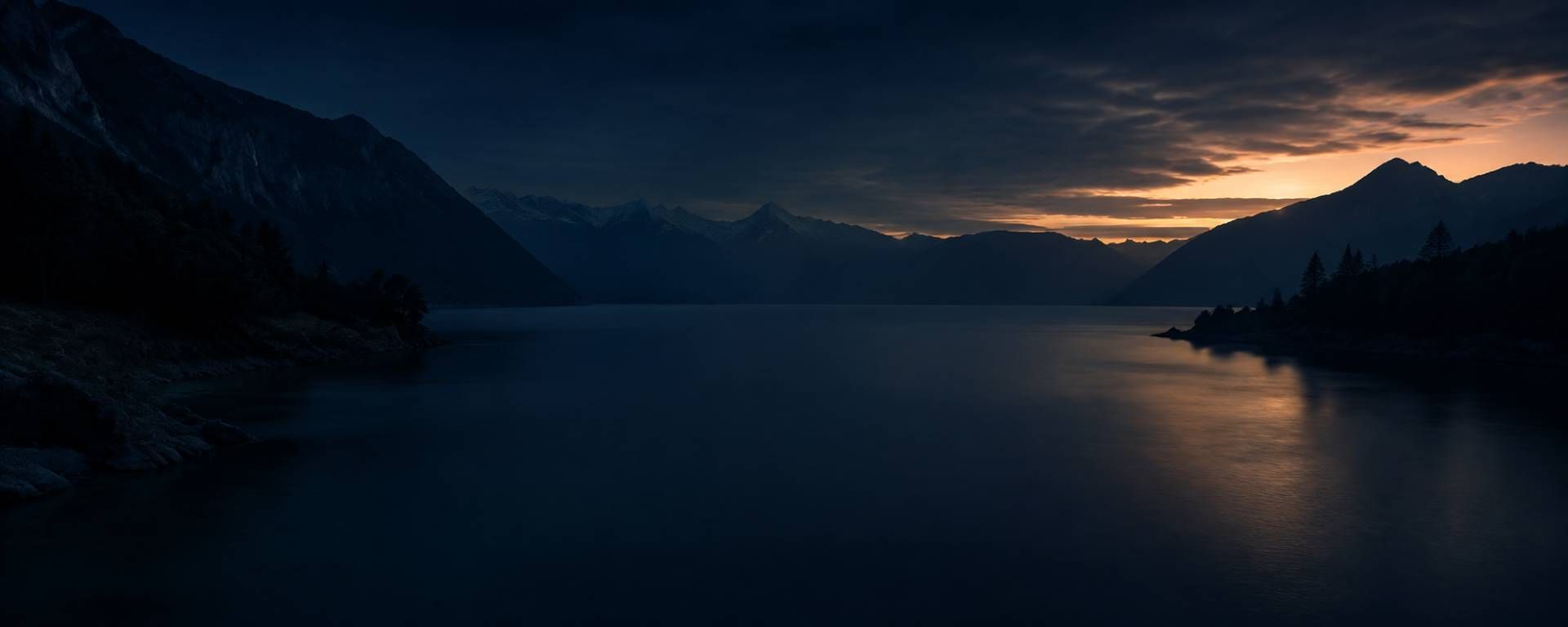 Dunkler Bergsee in der Abenddämmerung mit fernen, leuchtenden Stadtlichtern und einer ruhigen, spiegelnden Oberfläche