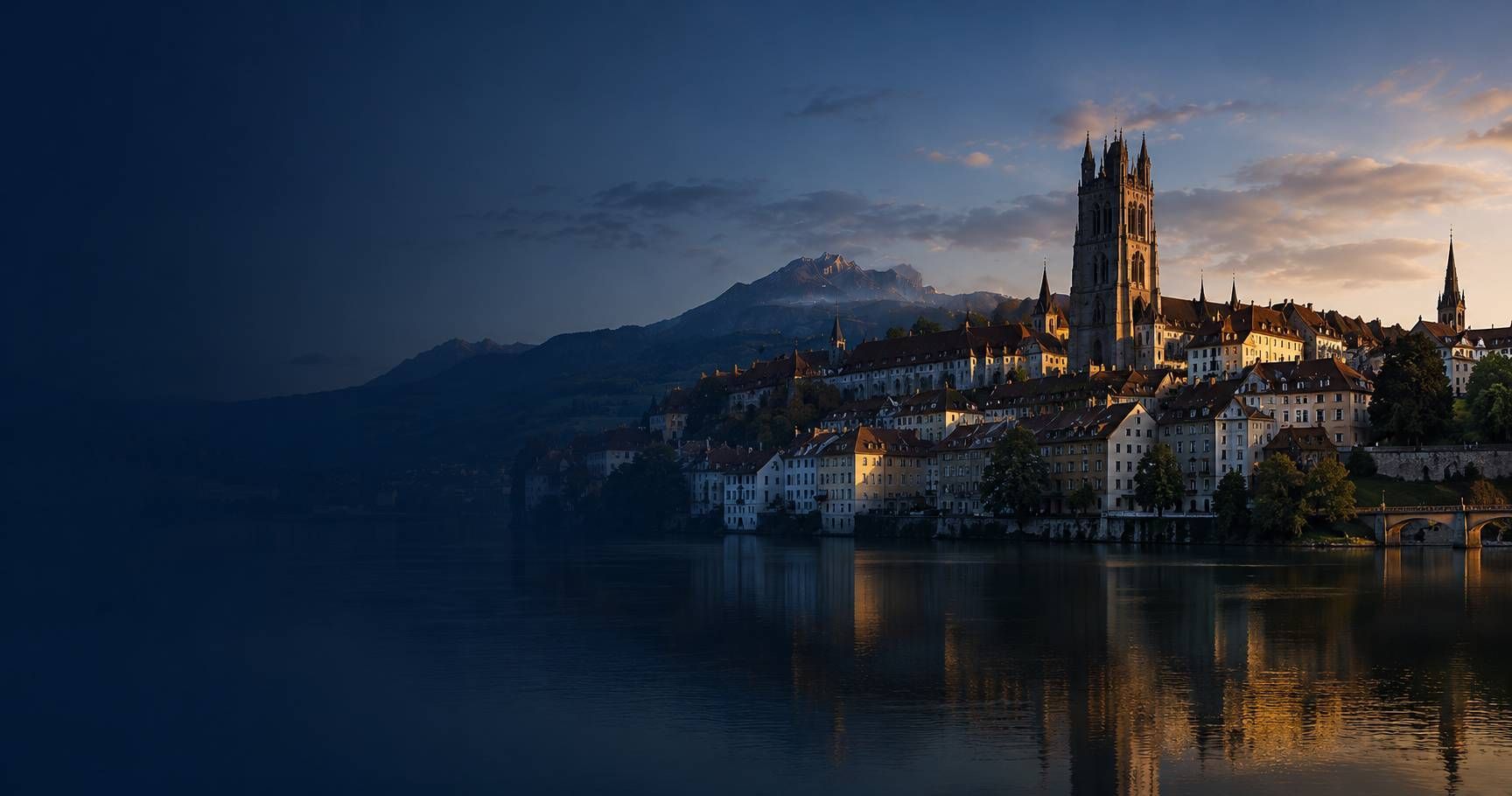 Sonnenuntergangsblick auf eine Stadt am See mit einer Kathedrale und Bergen, die sich im ruhigen Wasser spiegeln