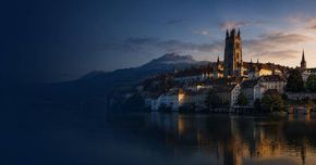 Sonnenuntergangsblick auf eine Stadt am See mit einer Kathedrale und Bergen, die sich im ruhigen Wasser spiegeln