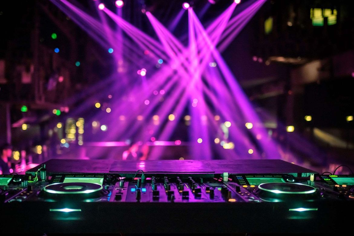 Un mezclador de DJ está sentado frente a un escenario con luces violetas saliendo de él.