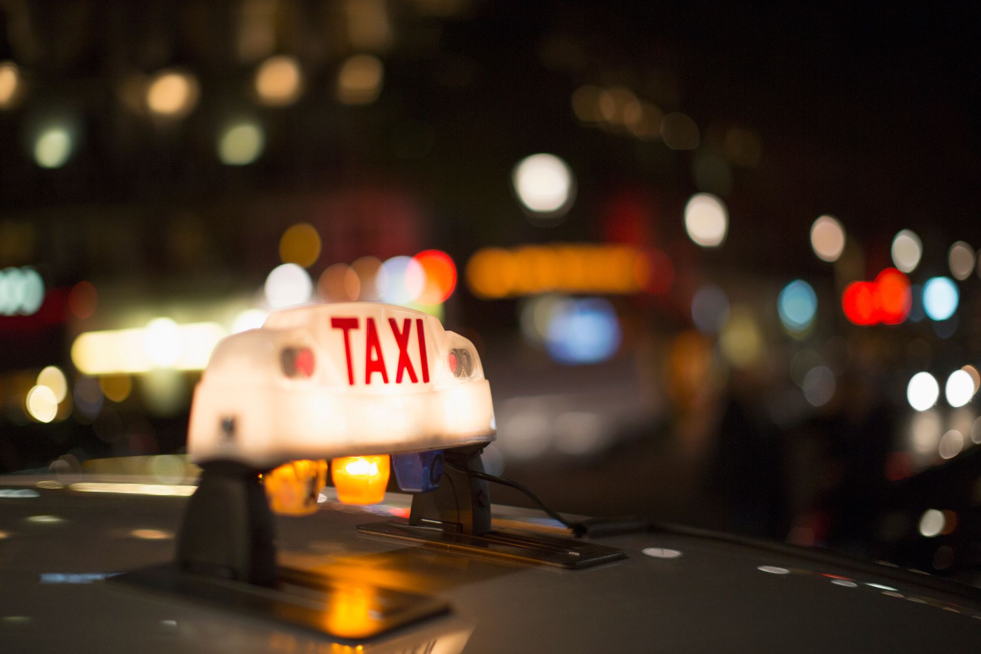 Panneau lumineux blanc sur le toit d'un taxi se détachant sur un fond de rue urbaine sombre et floue, la nuit.