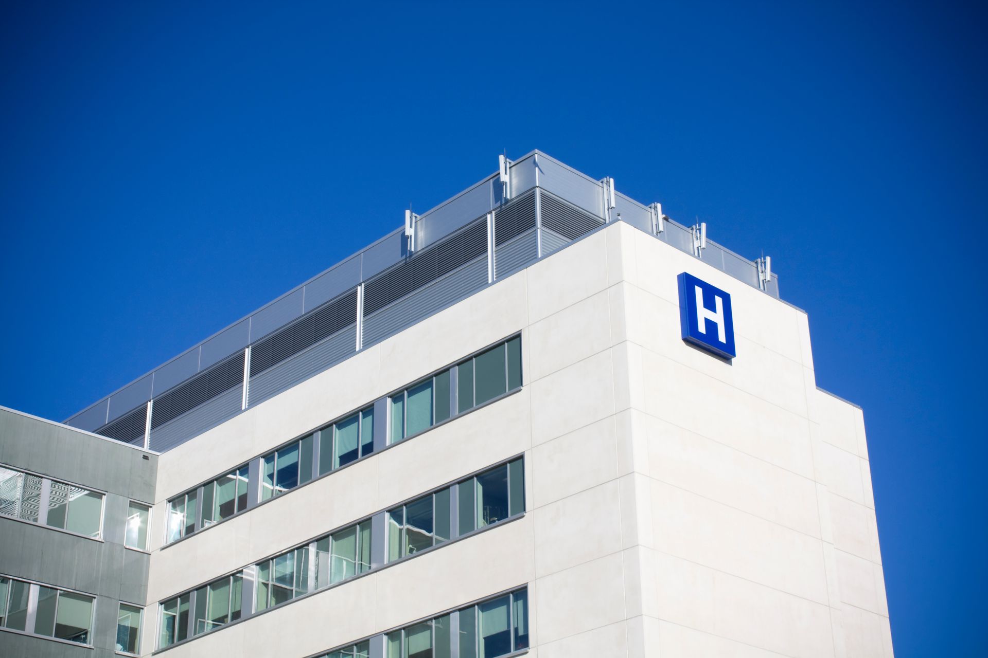 Un bâtiment hospitalier moderne et blanc, orné d'un H bleu, se détachant sur un ciel d'un bleu profond et limpide.