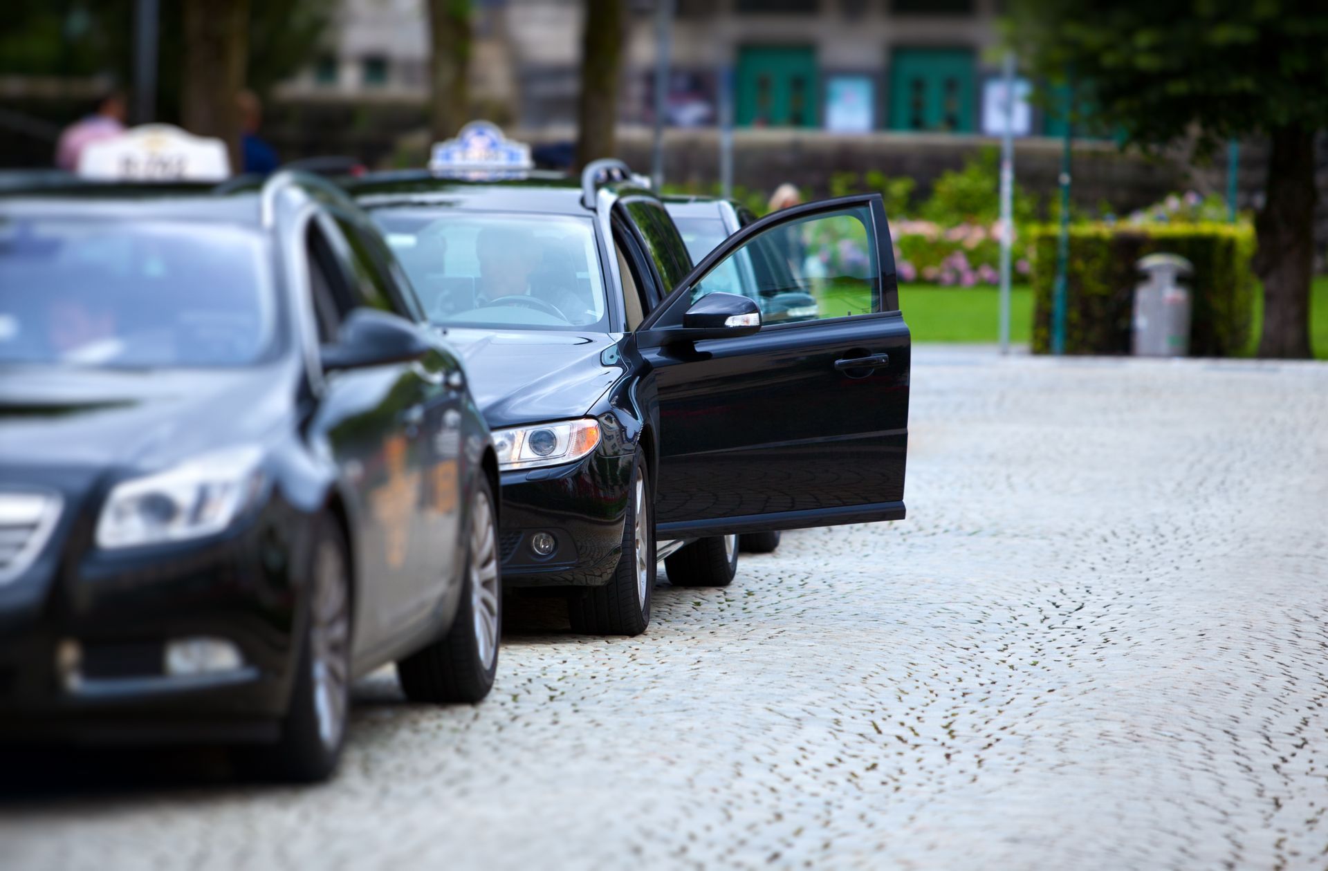 Deux taxis noirs stationnés sur une route pavée, l'un d'eux avec la portière côté conducteur ouverte.