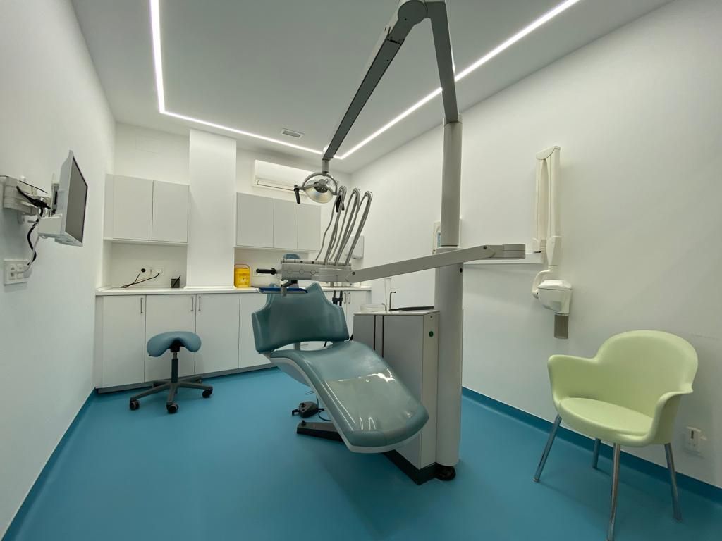 Clínica dental moderna con sillón, luz cenital, gabinetes y piso turquesa.