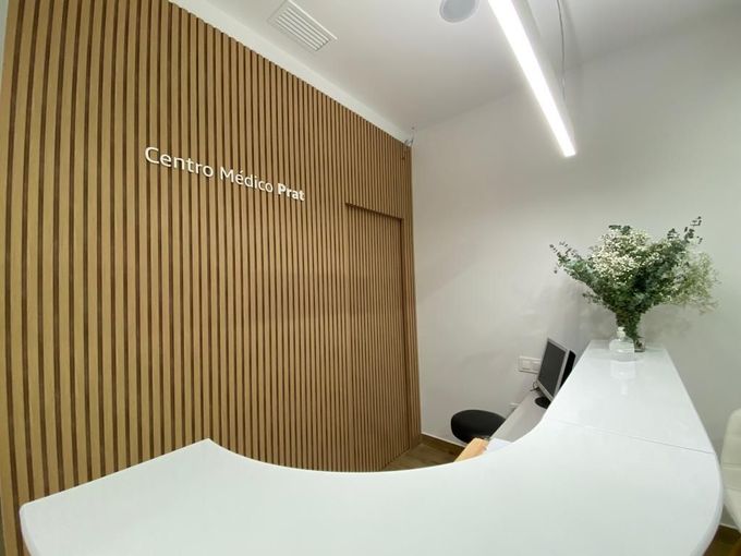 Mostrador de recepción moderno con pared de listones de madera, mostrador blanco y planta en un luminoso vestíbulo de oficina.