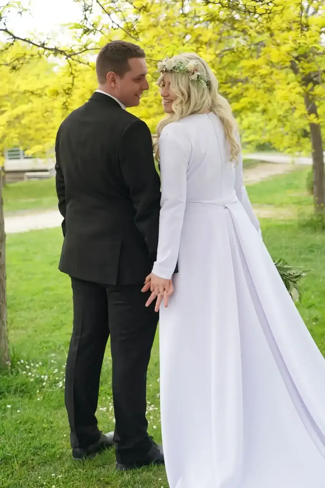Una pareja vestida de etiqueta posa junta al aire libre en un sendero cubierto de hierba